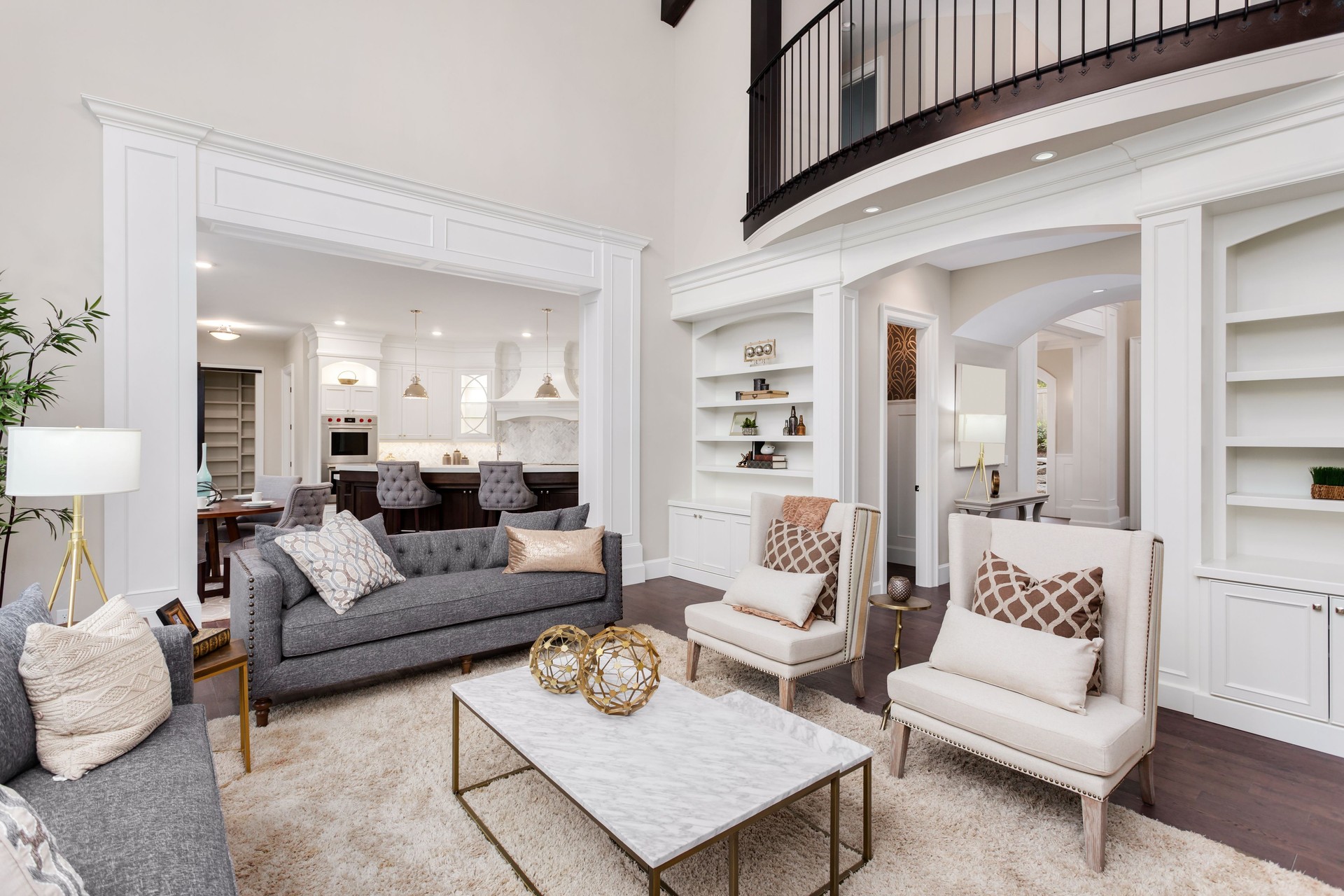 Beautiful living room interior with tall vaulted ceiling, loft area, hardwood floors and fireplace in new luxury home. Has view of kitchen and dining area, and loft.